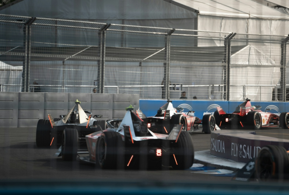 Formula E cars race through the indoor section of the London E‑Prix circuit at ExCeL London