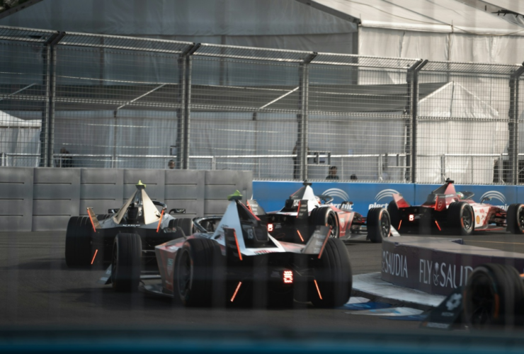 Formula E cars race through the indoor section of the London E‑Prix circuit at ExCeL London
