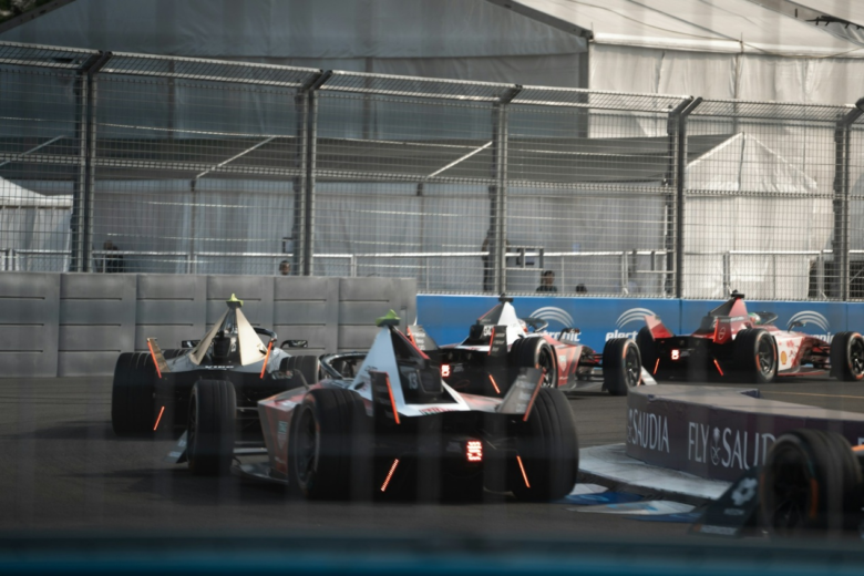 Formula E cars race through the indoor section of the London E‑Prix circuit at ExCeL London