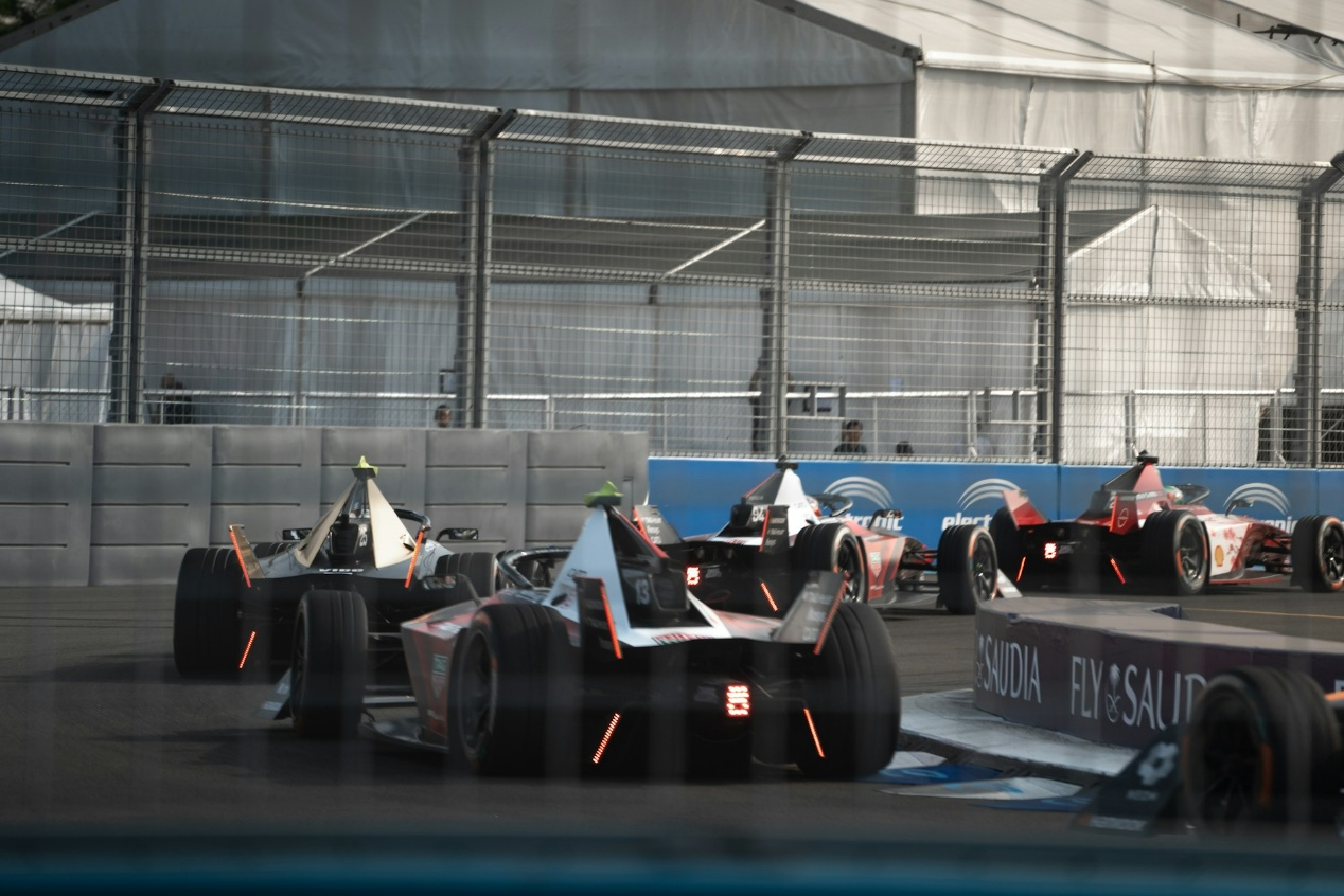 Formula E cars race through the indoor section of the London E‑Prix circuit at ExCeL London